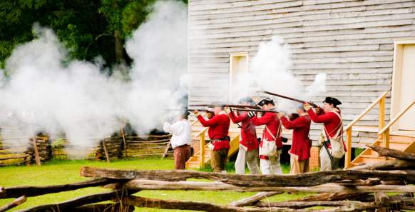 A live reenactment of a war with a wooden building in the background