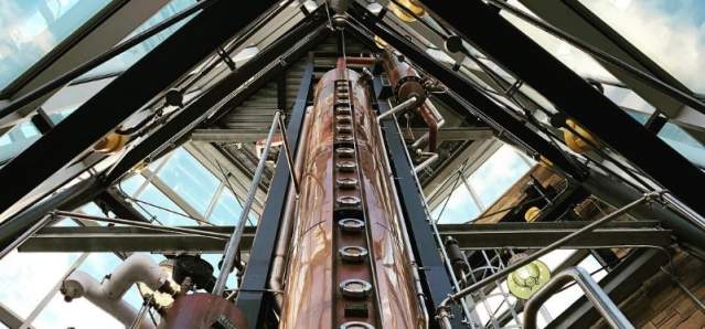A copper column still that's three stories high, surrounded by clear windows.