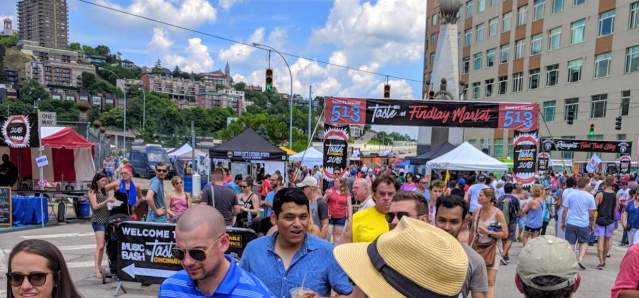 Taste of Cincinnati crowd in downtown Cincy headed under banner with blue sky and Mt. Adams in background