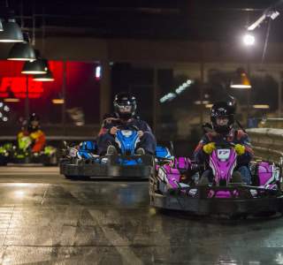 Drivers racing electric go-karts on an indoor track in Providence, Rhode Island, with colorful karts navigating a curve under overhead lights.