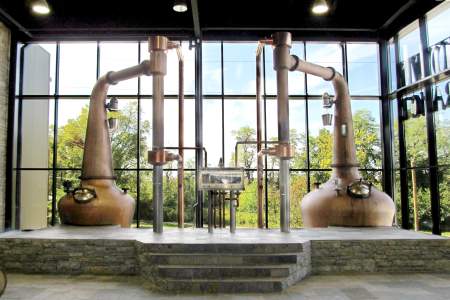 Two very large copper stills sit in front of a wall of windows at the Lexington Brewing and Distilling Co.