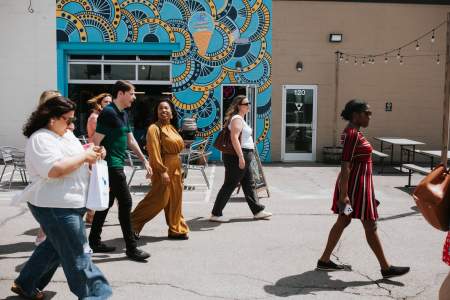 A group of four people walking past a vibrant blue and yellow patterned mural in the Lexington Distillery District on a sunny day.