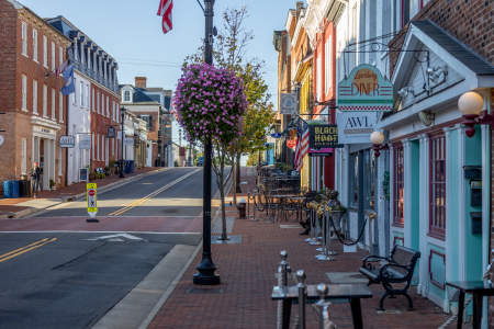 Downtown Leesburg's charming street scene featuring colorful storefronts, a diner sign, and hanging flower baskets. A quiet atmosphere with outdoor seating.