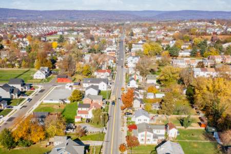 Aerial view of a Lovettsville, Virginia with tree-lined streets, houses, and autumn foliage under a clear blue sky. Scenic and inviting.