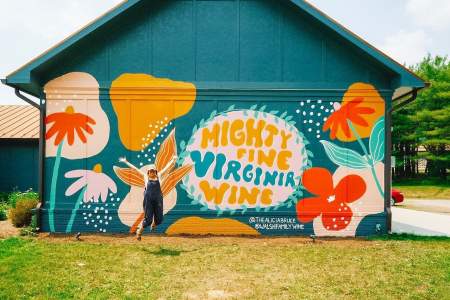 art mural that says "Mighty Fine Virginia Wine" with a woman jumping and smiling in front