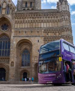 Lincoln Sightseeing bus outside Lincoln Cathedral in sunlight with people waiting to board.