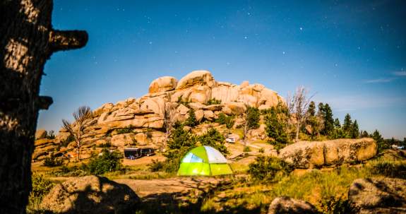 Green tent sits beneath a rock formation at Vedauwoo under a night sky full of stars.