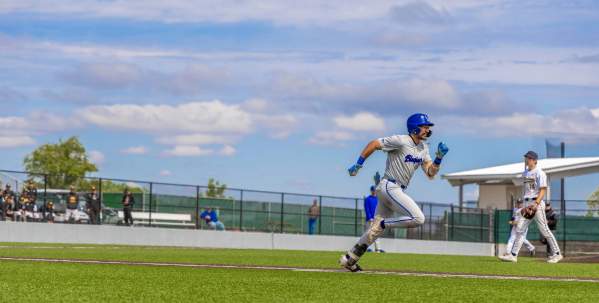 Baseball player running with another baseball player in the background.