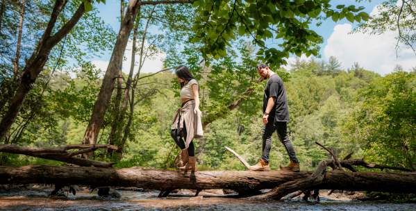 Man and Woman walking across a fallen tree over water