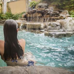 Back-shot of Woman Sipping Wine in Hot Tub with Rock Waterfall