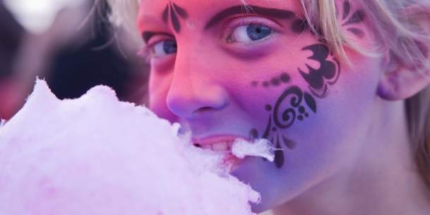 A girl with her face painted eating cotton candy