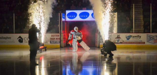 A goalie entering a darkened hockey arena while surrounded by a fireworks display.