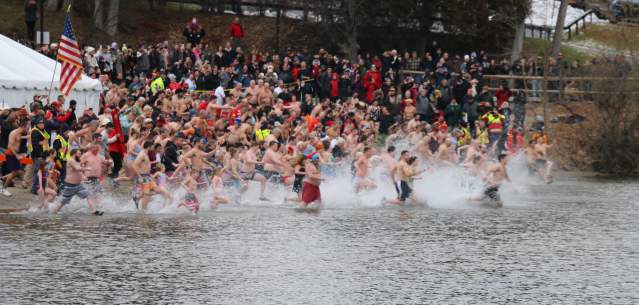 A crowd of swimmers running toward Lake George in winter for the polar plunge event.