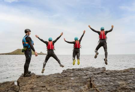 Group of people coasteering and jumping into water while instructor watches on