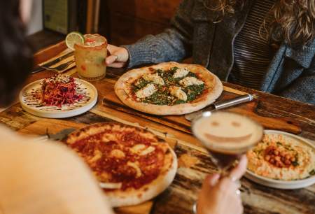 restaurant table filled with pizzas, vegan side dishes and drinks
