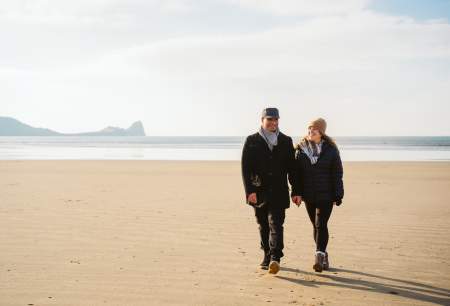A couple walking on Rhossili beach in the winter.