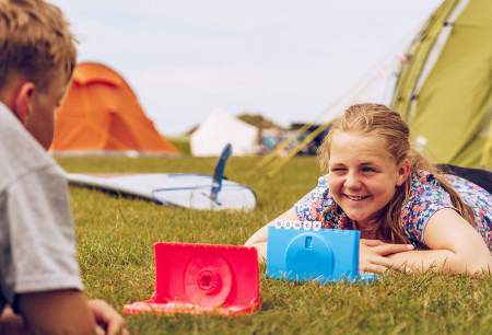A boy and a girl lying on the grass playing a game on a camp site.