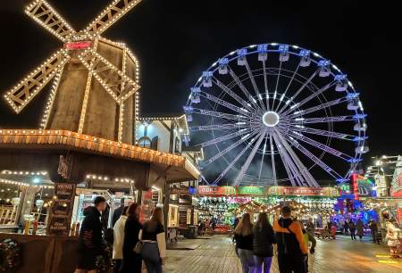 customers walking past stalls and big wheel at winter wonderland