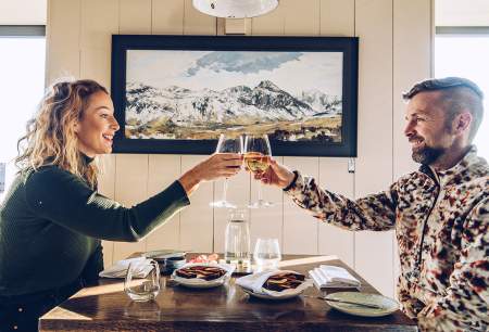 A man and a woman clinking glasses of wine over a table in a restaurant