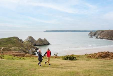 couple holding hands walking along three cliffs bay coastline