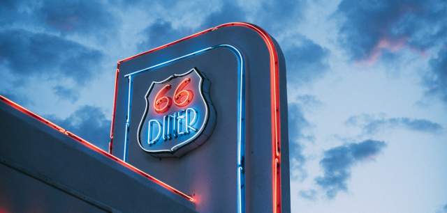 Neon sign for '66 Diner' illuminated in blue and red against a twilight sky with clouds.