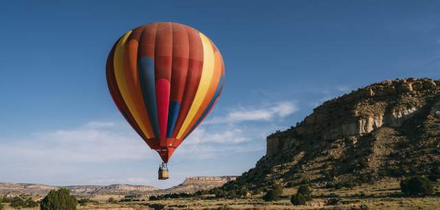 A colorful hot air balloon floats in a clear blue sky above a rugged landscape with rock formations.