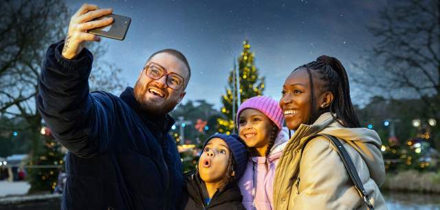 Family take a selfie photo with smartphone at Alton Towers with Christmas tree in the background