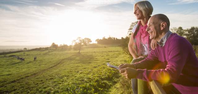 A couple leans on a wooden fence and admire the view, as the sun starts to set