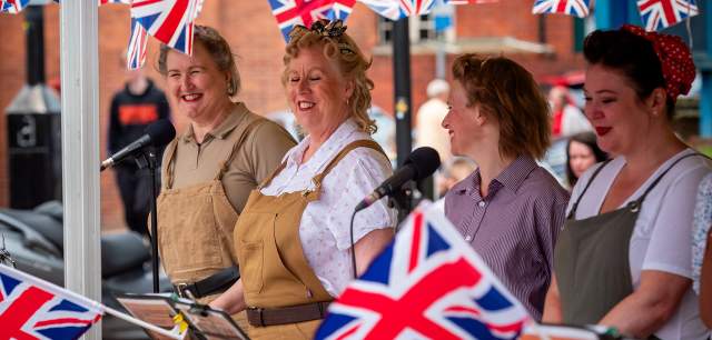 Group of women in vintage costumes surrounded by Union Jack flag bunting
