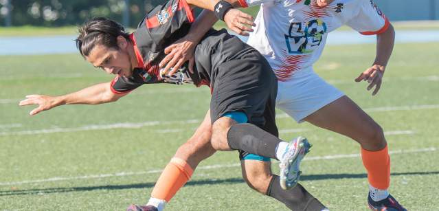 Two male soccer players fighting for a soccer ball on a soccer field.