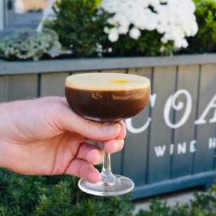 Hand holding Coast espresso martini outside Coast Wine House in Dublin, Ohio, with white flowers in the background.