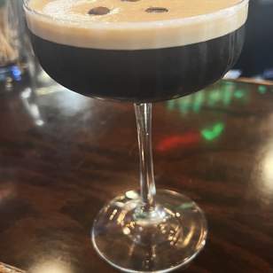 Close-up of Dublin Village Tavern's Espresso Patronum martini topped with three coffee beans on a dark wooden bar.
