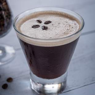 Close-up of Fado Signature espresso martini garnished with three coffee beans on a wood table.