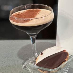 Modern Male Espresso martini with cocoa dusting served with a black and white cookie on a glass dish.