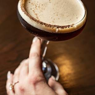 Hand holding Cold Brew espresso martini with chocolate rim on dark wood table at Rusty Bucket in Dublin, Ohio.
