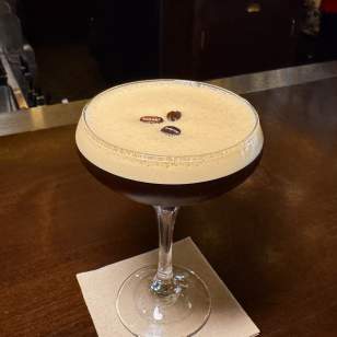 Espresso martini topped with three coffee beans served on a cocktail napkin at The Avenue in Dublin, Ohio.