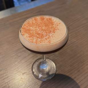 Espresso martini with cinnamon garnish served in a coupe glass on a wooden bar at The Pearl in Dublin, Ohio.