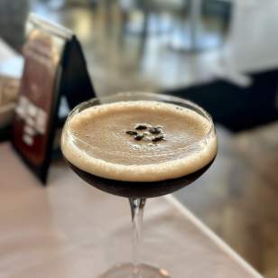 Close-up of Tucci's espresso martini garnished with coffee beans, served in a coupe glass on a table.