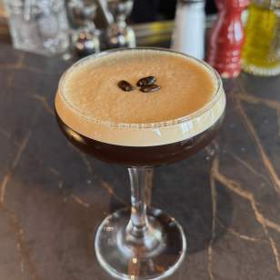 Espresso martini garnished with three coffee beans on a dark marble bar counter at Valentina’s in Dublin, Ohio.