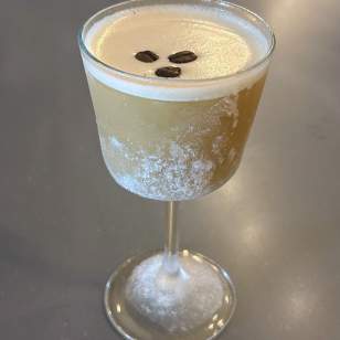 Frozen espresso martini in a frosted glass garnished with three coffee beans on a gray background.