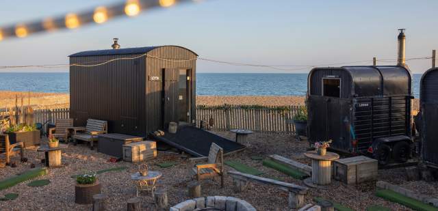 Two sauna sheds on the shingle beach, surrounding a campfire in Brighton