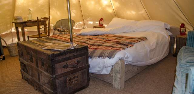 A double bed and antique furniture inside a bell tent at Knepp, Sussex