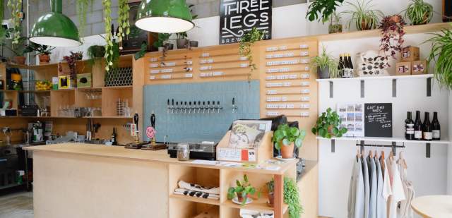 A wooden bar area with hanging lights and plants at Three Legs Brewery