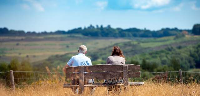 Two people sitting on a bench looking out on the rolling hills and woodland at Ashdown Forest, East Sussex