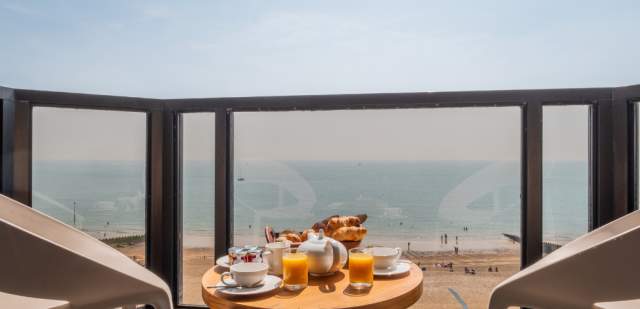 a balcony room at The View hotel in Eastbourne. There is a breakfast on the table, two chairs and a view over the sea and beach