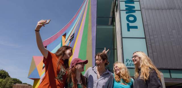 A group of young people take their photo in front of the colourful exterior of Towner gallery, Eastbourne