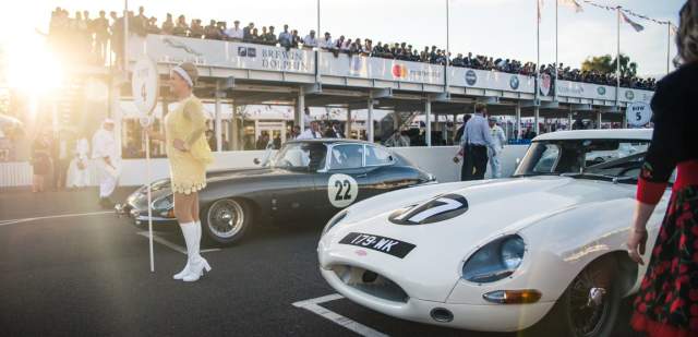 Two cars on the start line at the vintage car festival with crowds in pit lane and grandstand, Goodwood Revival
