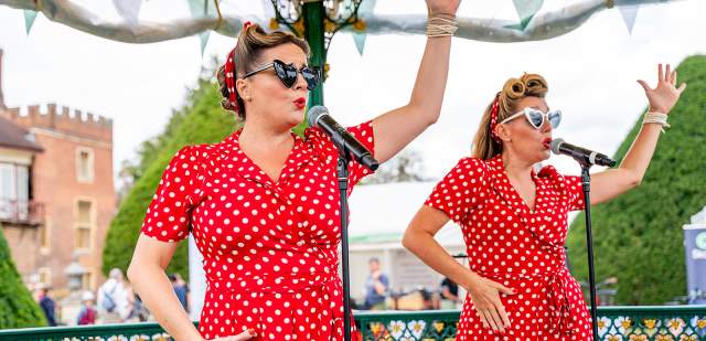 Two ladies wearing red polka dot dresses sing on a bandstand in Sussex