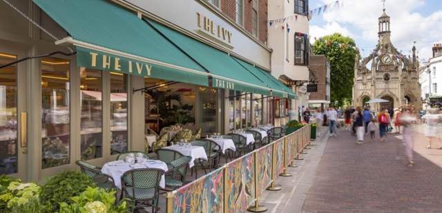External The Ivy Chichester with green canopies, outdoor seating and the clock tower in the distance