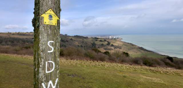 A wooden signpost with a yellow arrow for the South Downs Way, in Eastbourne